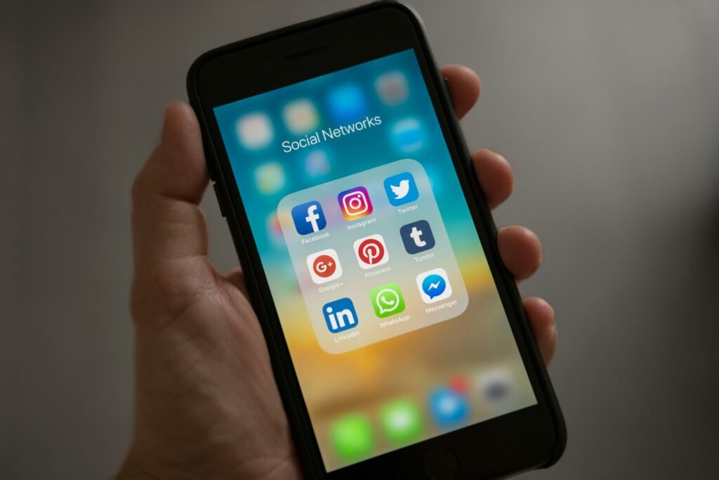 A smartphone displaying various social media services icons held in a hand, showcasing modern communication apps.